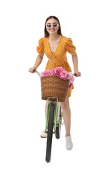 Smiling woman in sunglasses riding bicycle with basket of peony flowers on white background