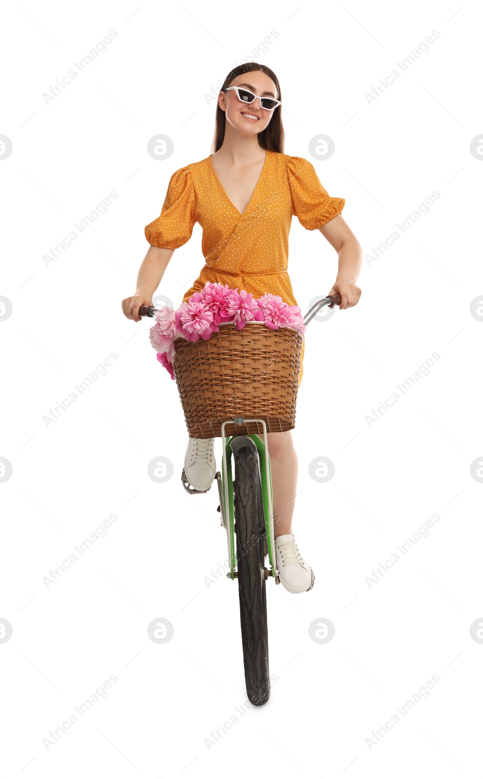 Photo of Smiling woman in sunglasses riding bicycle with basket of peony flowers on white background