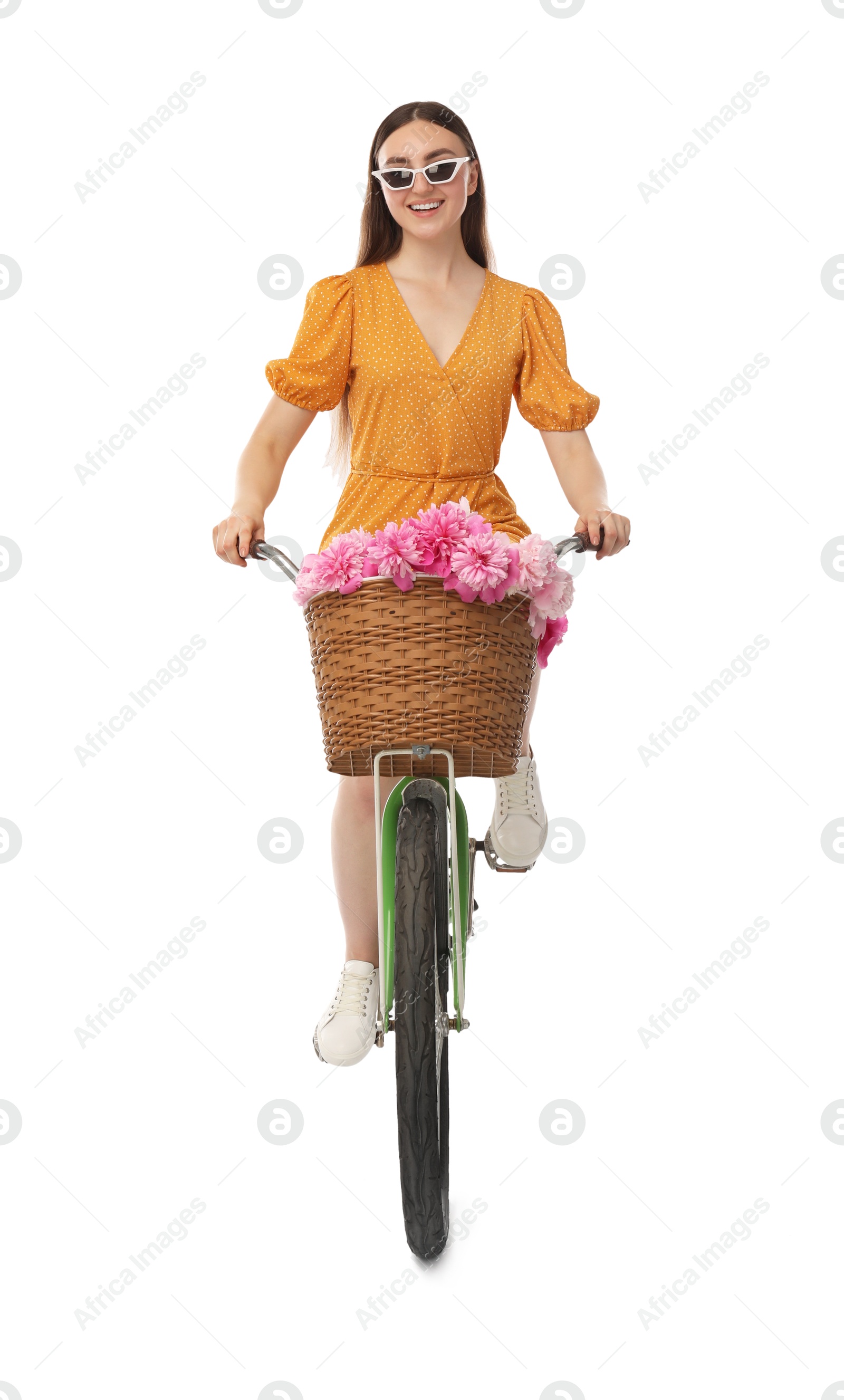 Photo of Smiling woman in sunglasses riding bicycle with basket of peony flowers on white background