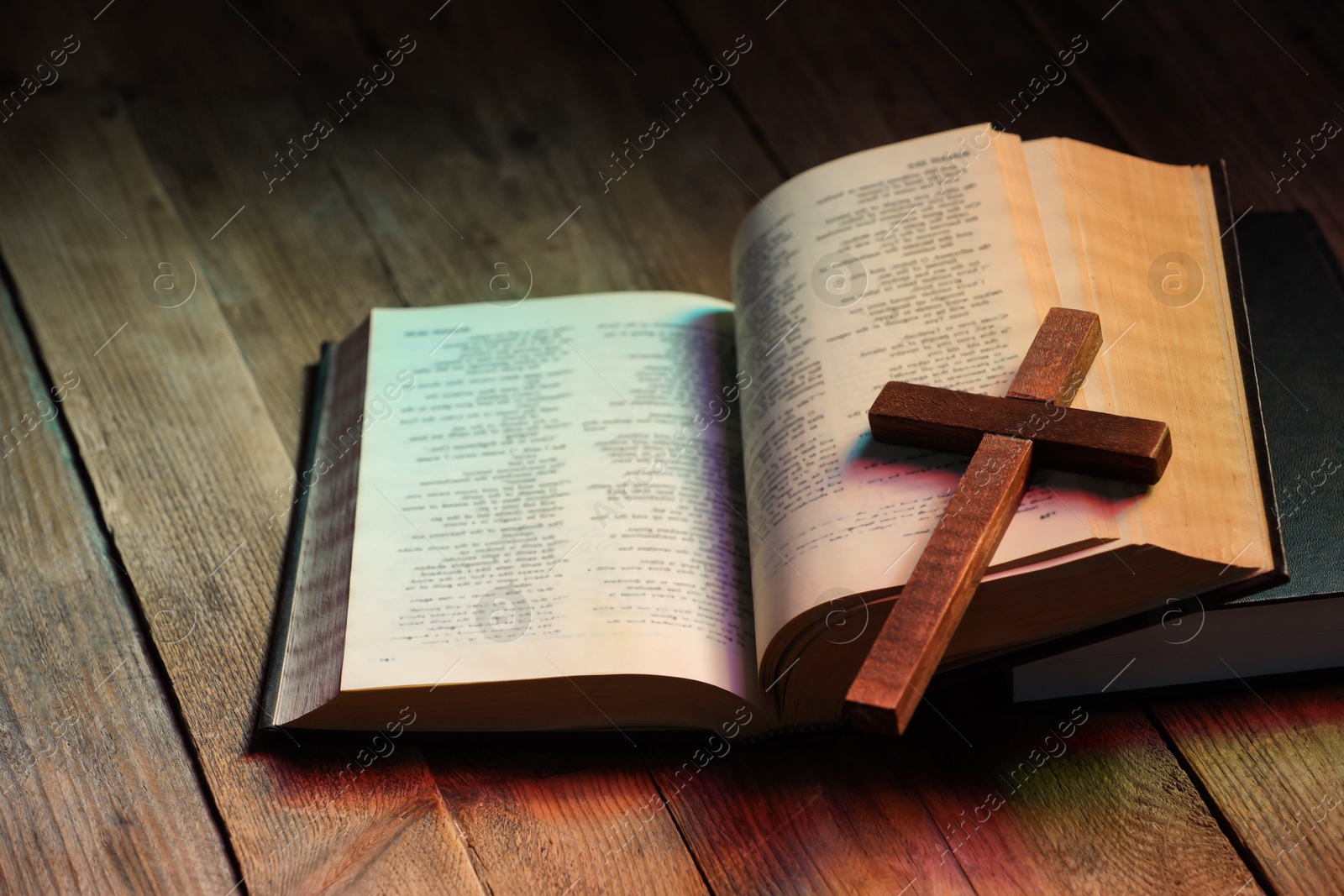 Photo of Cross and Bible on wooden table in color lights, closeup. Religion of Christianity