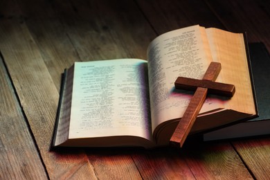 Photo of Cross and Bible on wooden table in color lights, closeup. Religion of Christianity