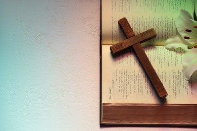 Photo of Wooden cross, Bible and lily flower on textured table in color lights, top view with space for text. Religion of Christianity