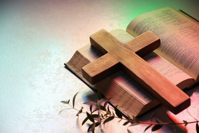 Photo of Wooden cross, Bible and eucalyptus branch on textured table in color lights, closeup with space for text. Religion of Christianity