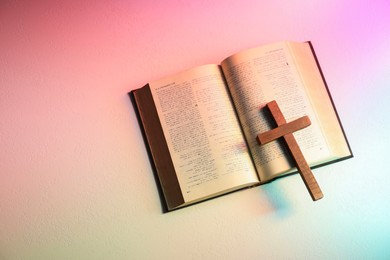 Bible and wooden cross on textured table in color lights, top view with space for text. Religion of Christianity