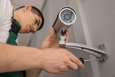 Technician with screwdriver installing CCTV camera on wall indoors, low angle view and selective focus