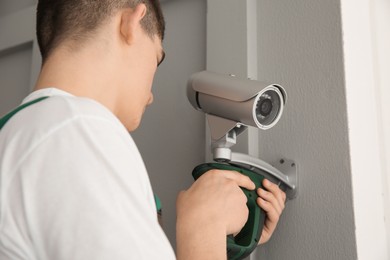 Technician with cordless electric screwdriver installing CCTV camera on wall indoors