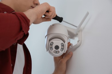 Photo of Technician with screwdriver installing CCTV camera on wall indoors, closeup