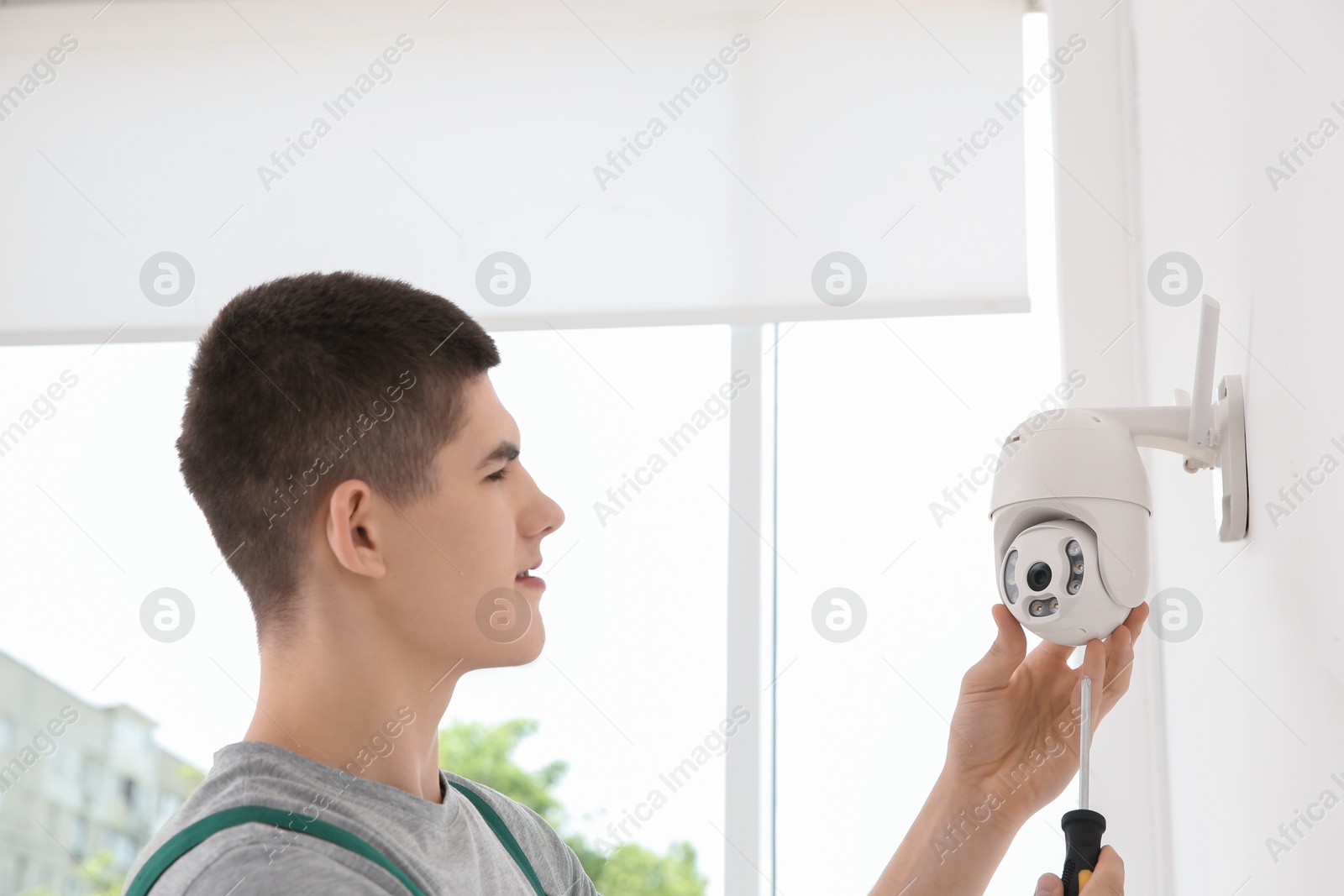 Photo of Technician with screwdriver installing CCTV camera on wall indoors