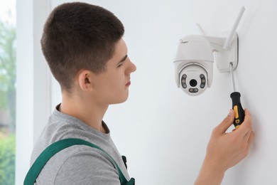 Technician with screwdriver installing CCTV camera on wall indoors