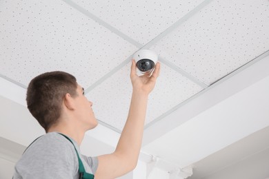 Technician installing CCTV camera on ceiling indoors, low angle view