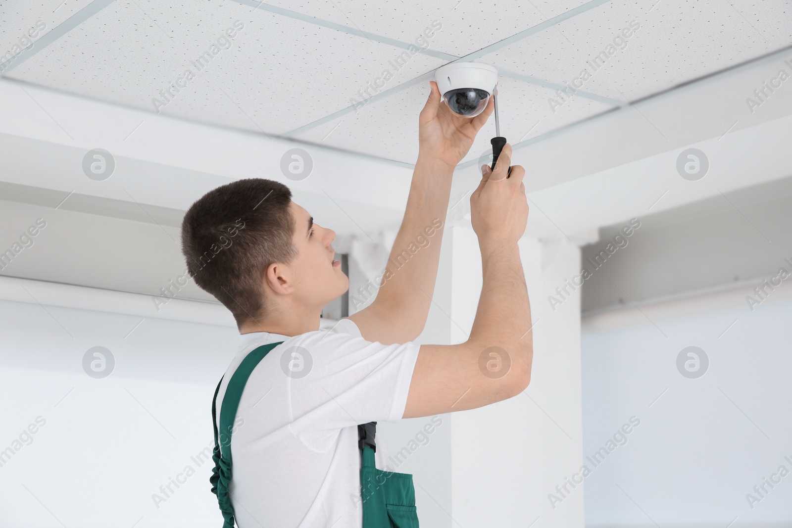 Photo of Technician with screwdriver installing CCTV camera on ceiling indoors