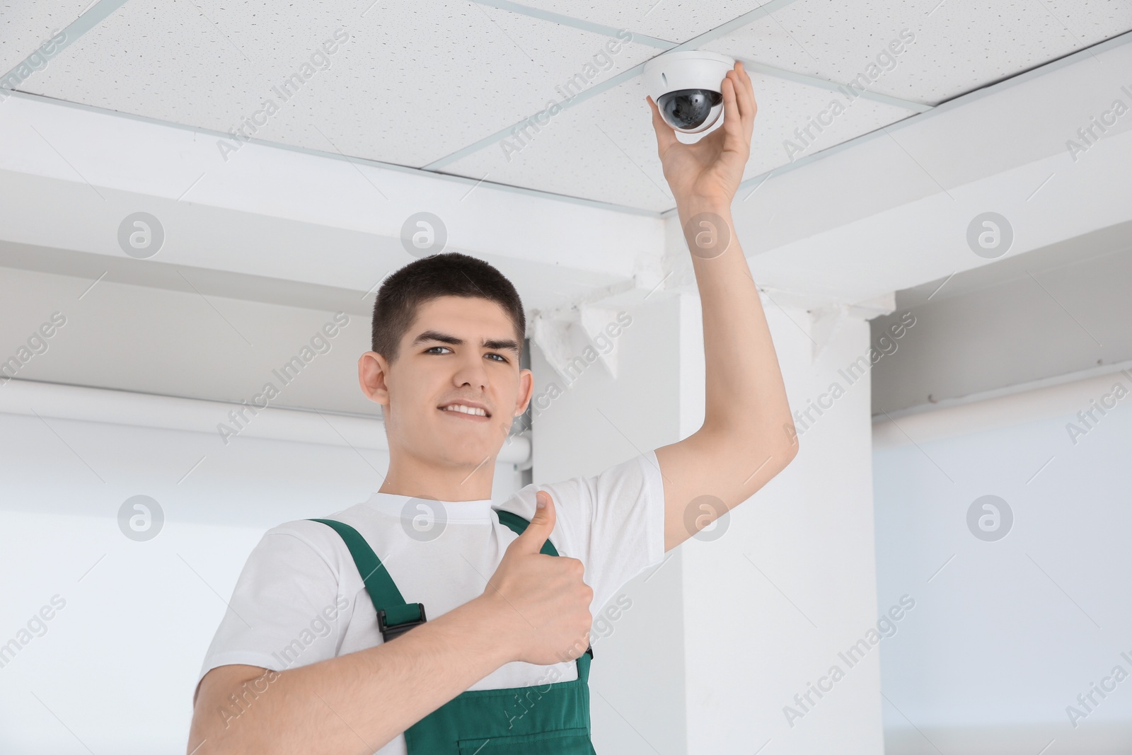 Photo of Technician showing thumbs up while installing CCTV camera on ceiling indoors