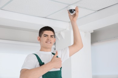 Technician showing thumbs up while installing CCTV camera on ceiling indoors