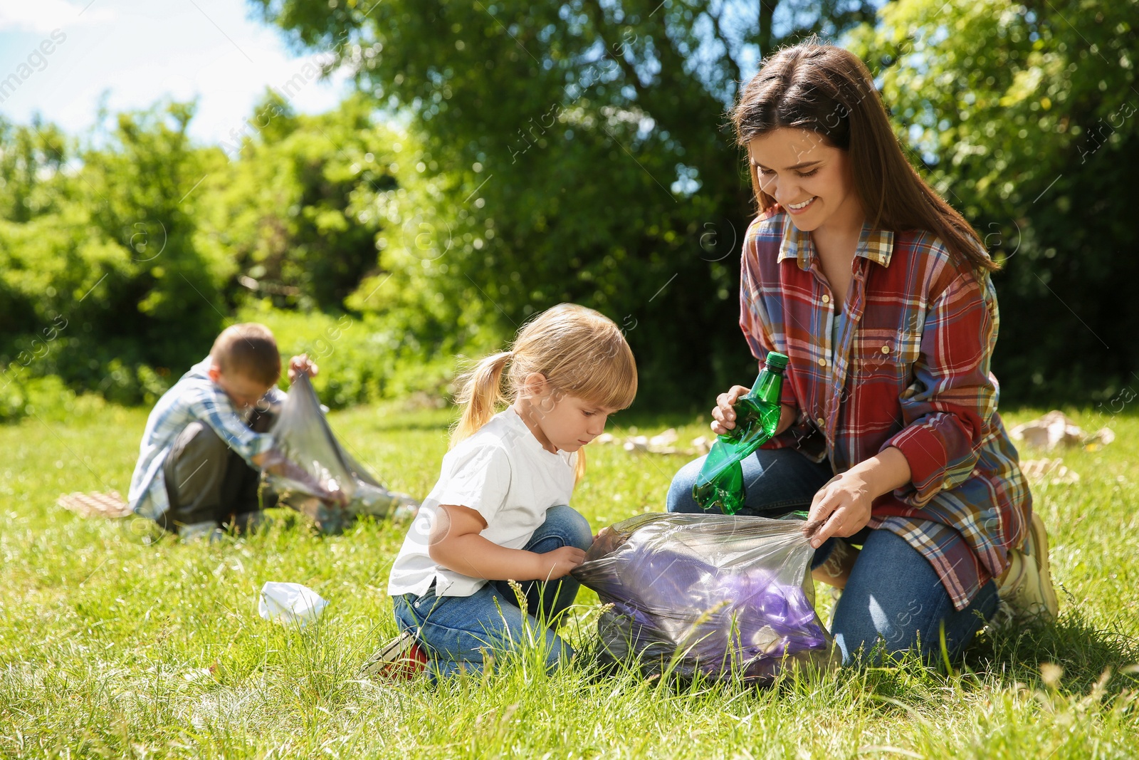 Photo of Mother and her children with plastic bags collecting garbage in park