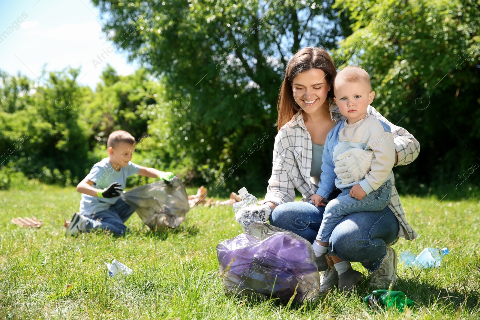 Photo of Mother and her children with plastic bags collecting garbage in park