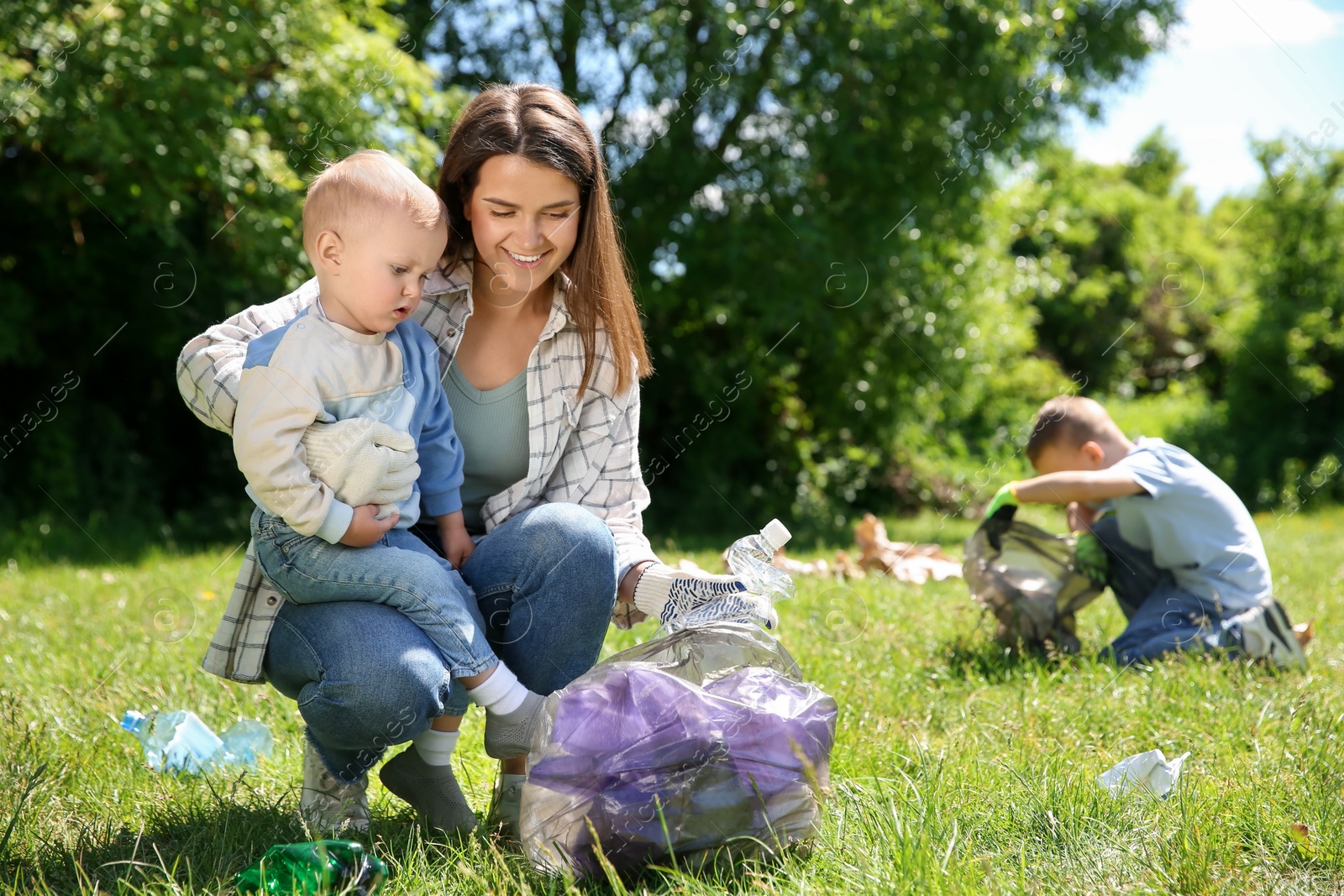 Photo of Mother and her children with plastic bags collecting garbage in park