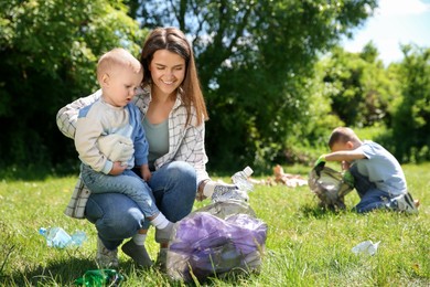 Photo of Mother and her children with plastic bags collecting garbage in park