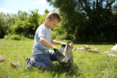 Photo of Little boy with plastic bag collecting garbage in park