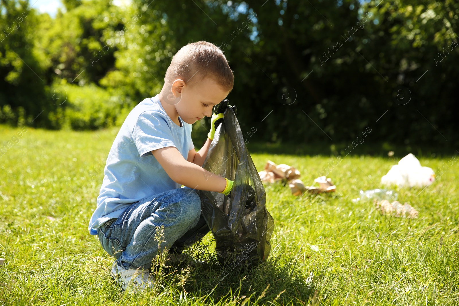 Photo of Little boy with plastic bag collecting garbage in park