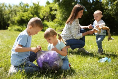 Photo of Mother and her children with plastic bags collecting garbage in park