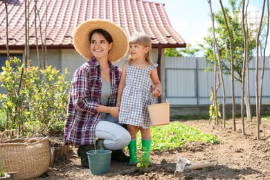 Mother and her cute daughter planting tree together in garden