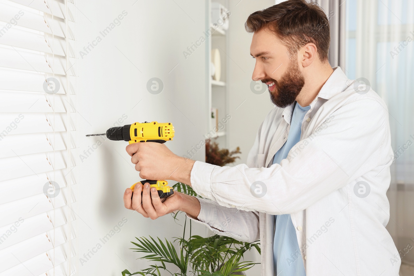 Photo of Smiling man drilling white wall at home