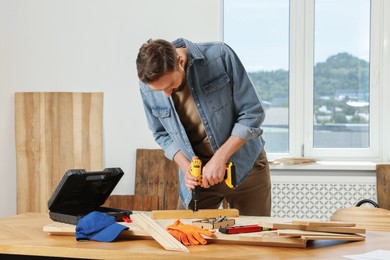 Photo of Craftsman working with drill at wooden table in workshop