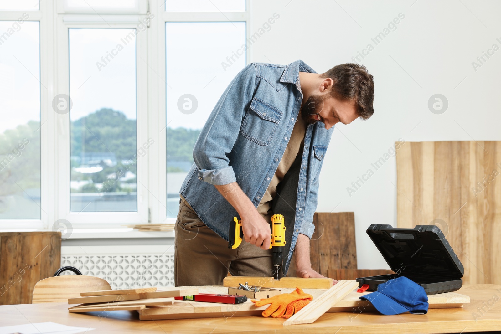 Photo of Smiling craftsman working with drill at wooden table in workshop