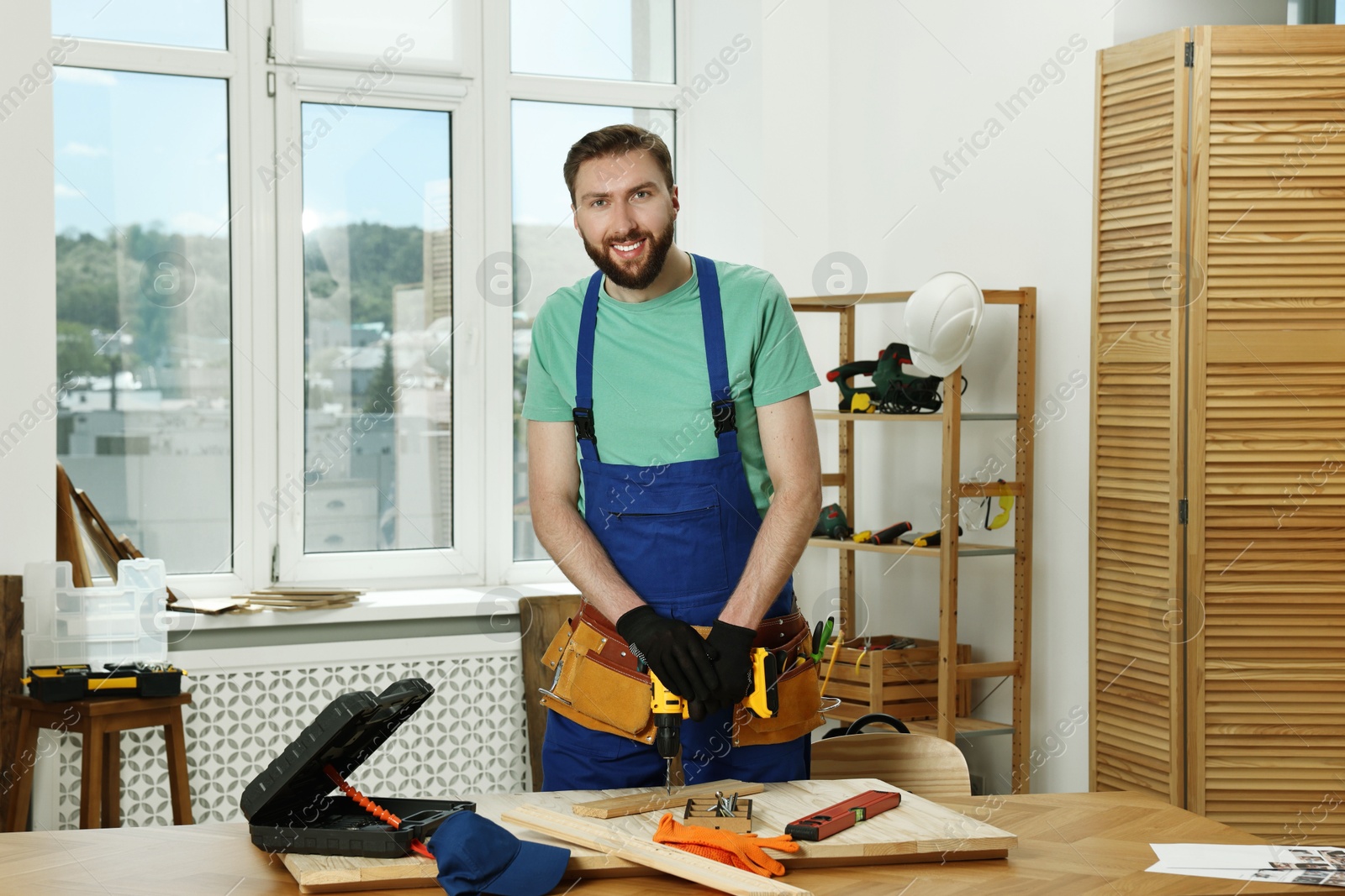 Photo of Portrait of smiling craftsman with drill at table in workshop
