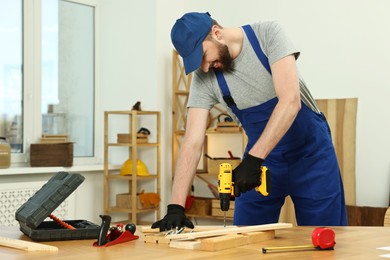 Photo of Smiling craftsman working with drill at table in workshop