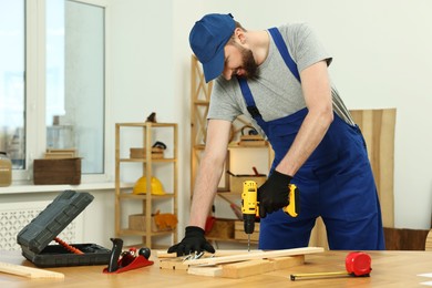 Smiling craftsman working with drill at table in workshop