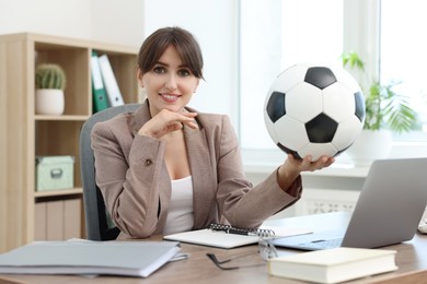 Smiling employee with soccer ball at table in office