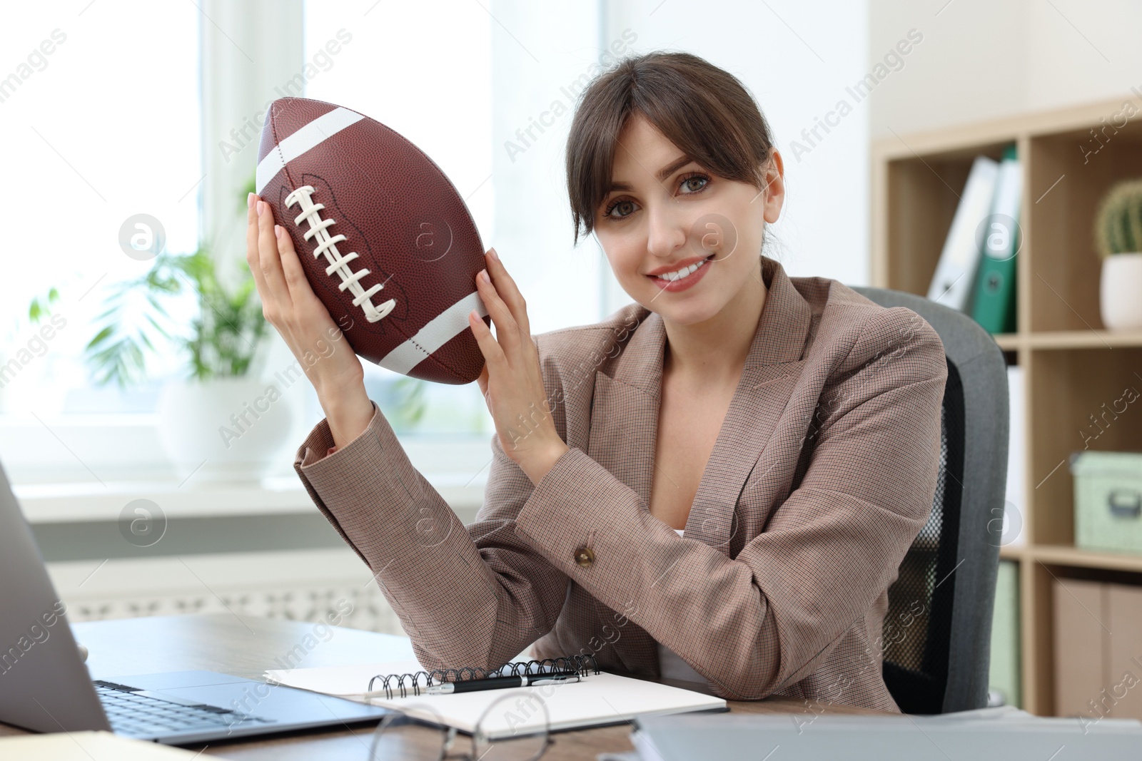 Photo of Smiling employee with american football ball at table in office