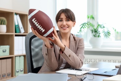 Smiling employee with american football ball at table in office