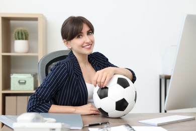 Smiling employee with soccer ball at table in office