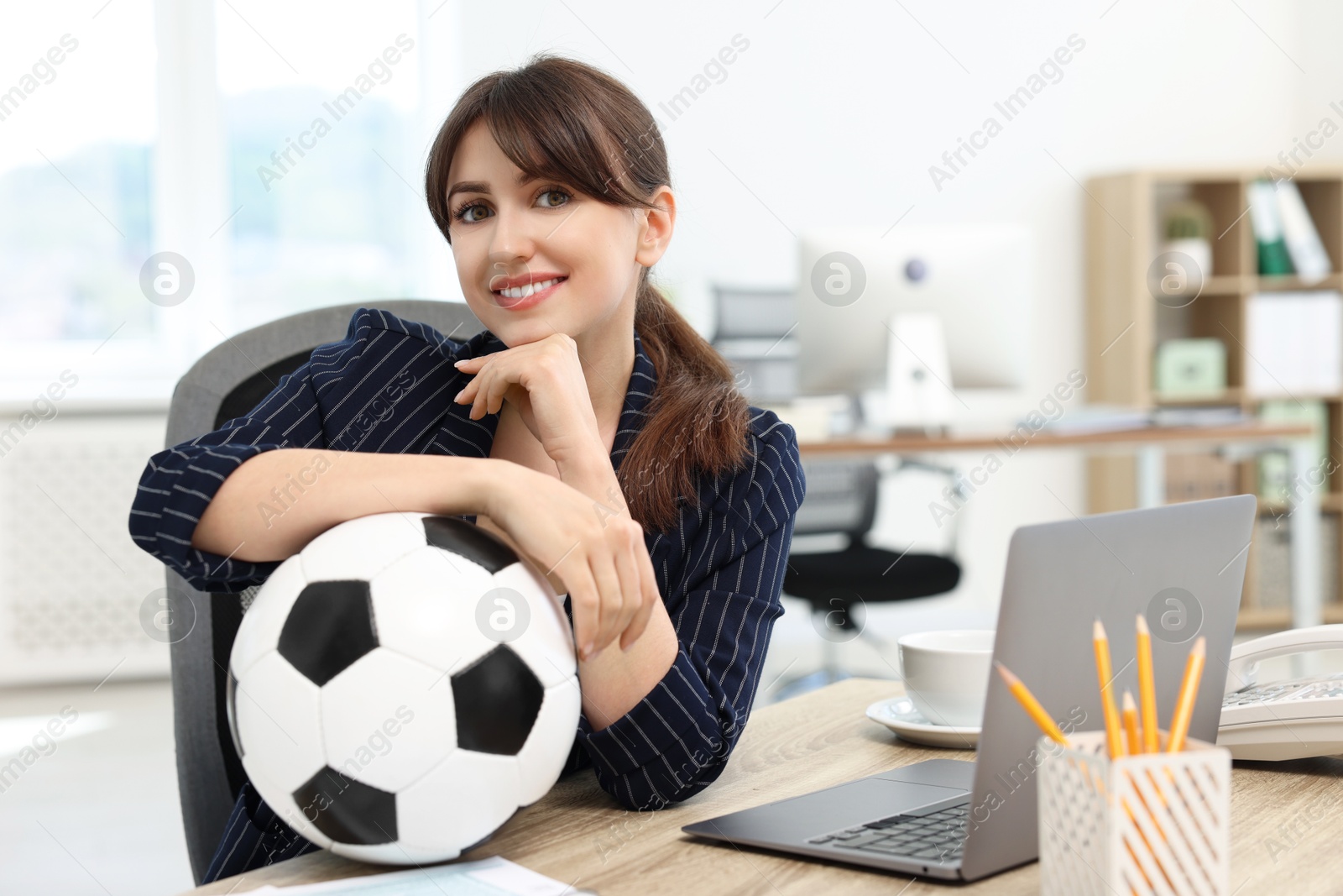 Photo of Smiling employee with soccer ball at table in office