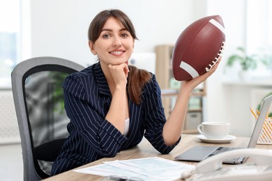 Smiling employee with american football ball at table in office