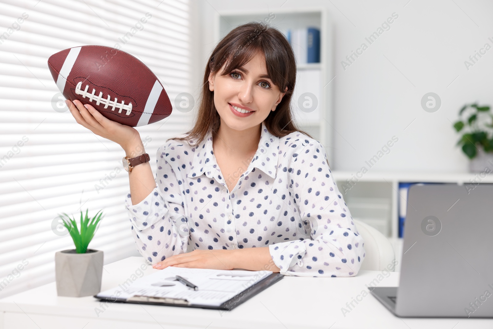 Photo of Smiling employee with american football ball at table in office