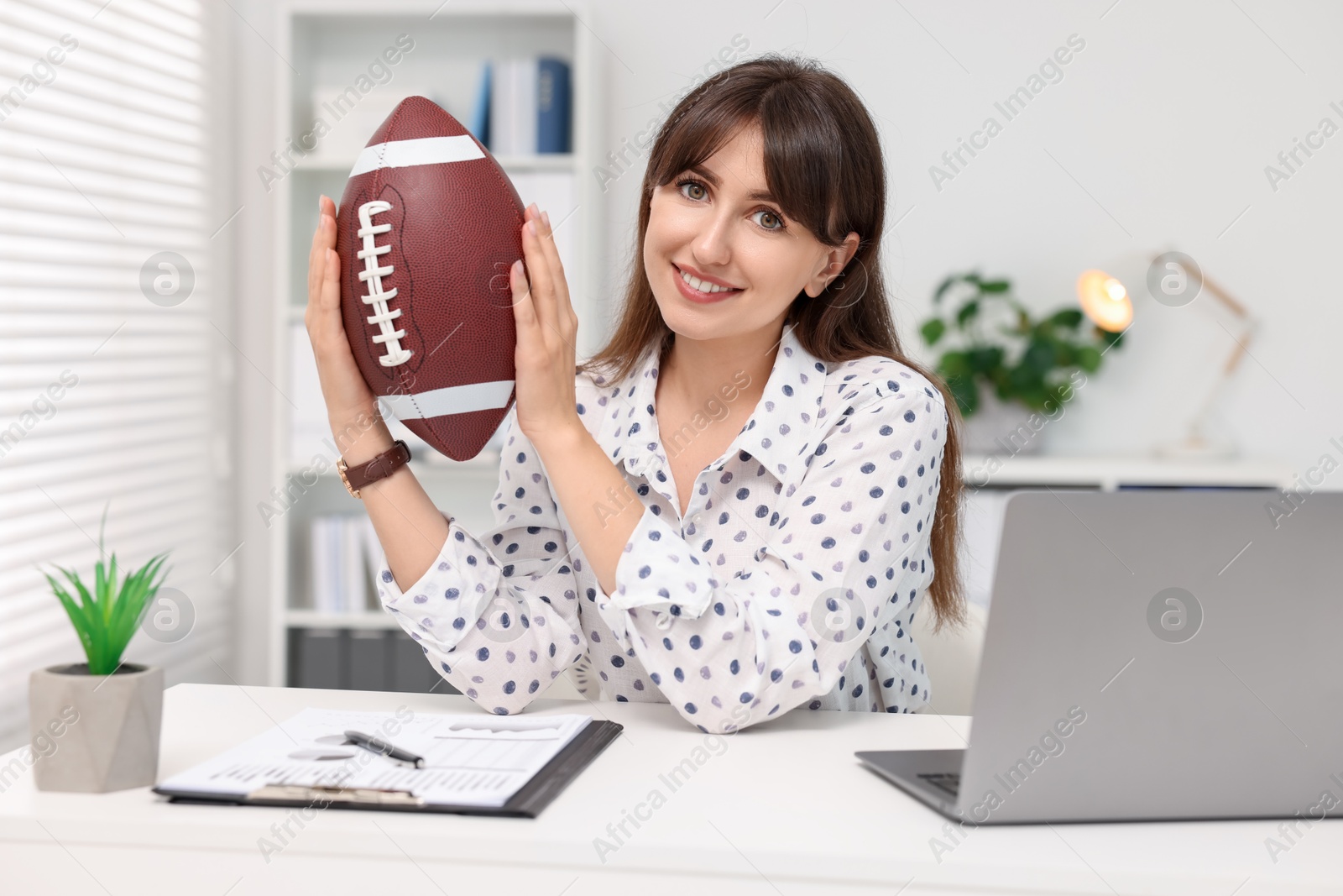 Photo of Smiling employee with american football ball at table in office