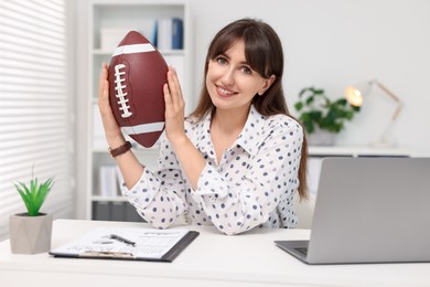 Smiling employee with american football ball at table in office