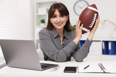 Photo of Smiling employee with american football ball at table in office