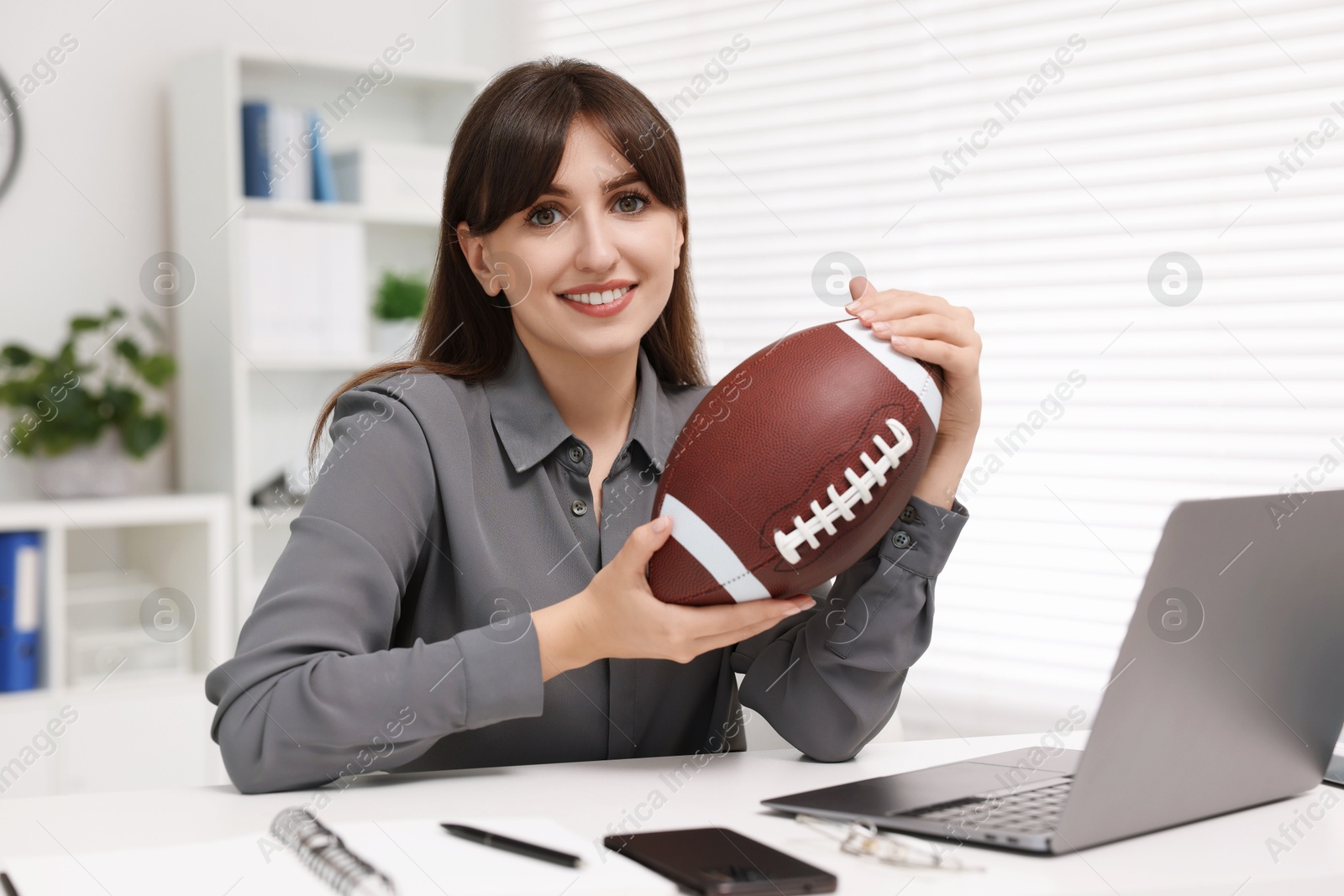 Photo of Smiling employee with american football ball at table in office