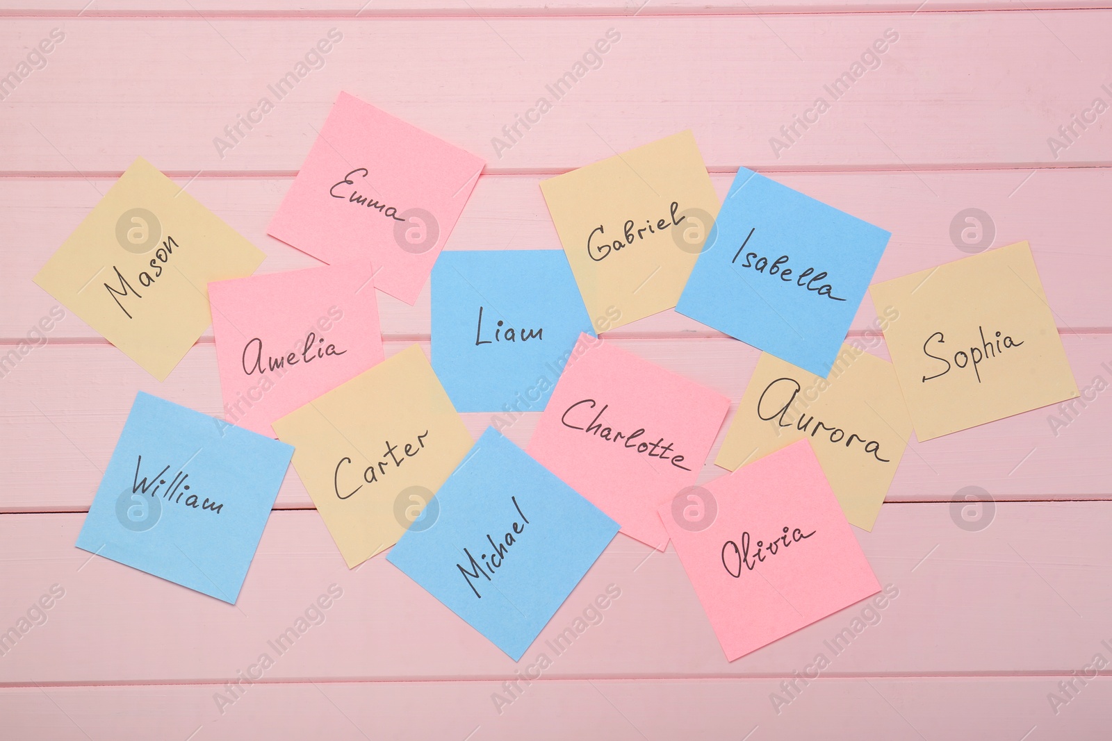 Photo of Paper stickers with different names on pink wooden background, flat lay. Choosing baby's name