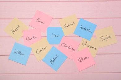 Photo of Paper stickers with different names on pink wooden background, flat lay. Choosing baby's name