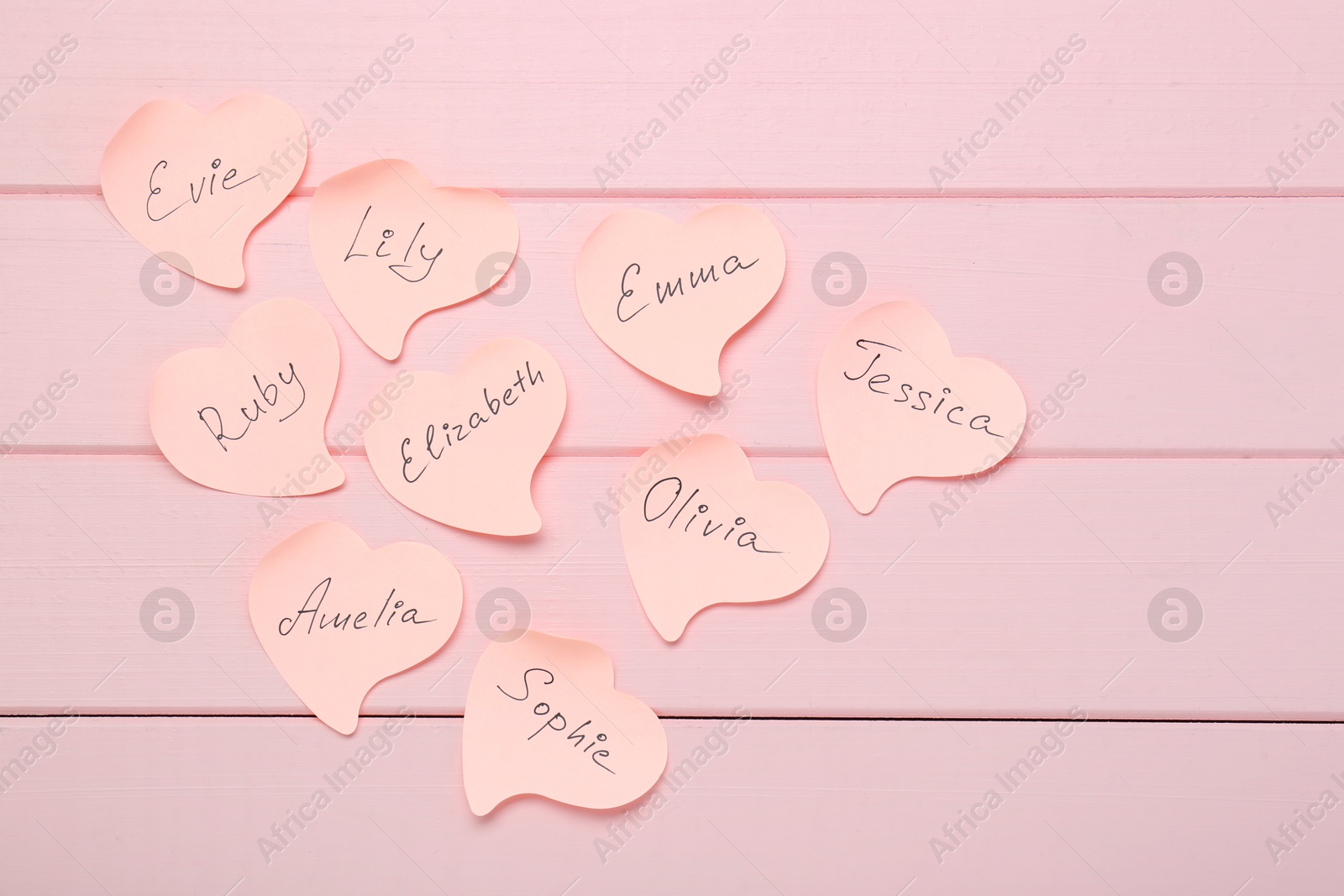 Photo of Paper stickers with different names on pink wooden background, flat lay. Choosing baby's name