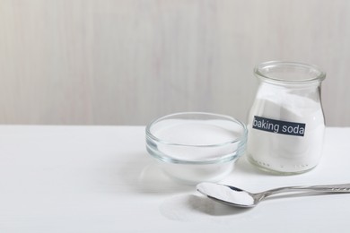 Photo of Baking soda in bowl, glass jar and spoon on white wooden table, space for text