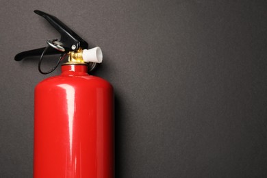 One red fire extinguisher on dark gray background, top view. Space for text