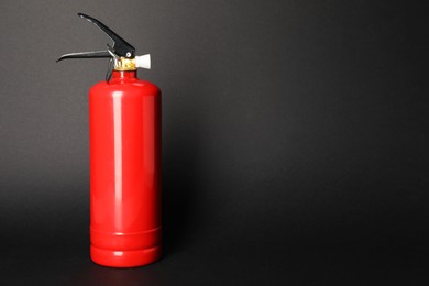 Photo of One red fire extinguisher on dark gray background, space for text