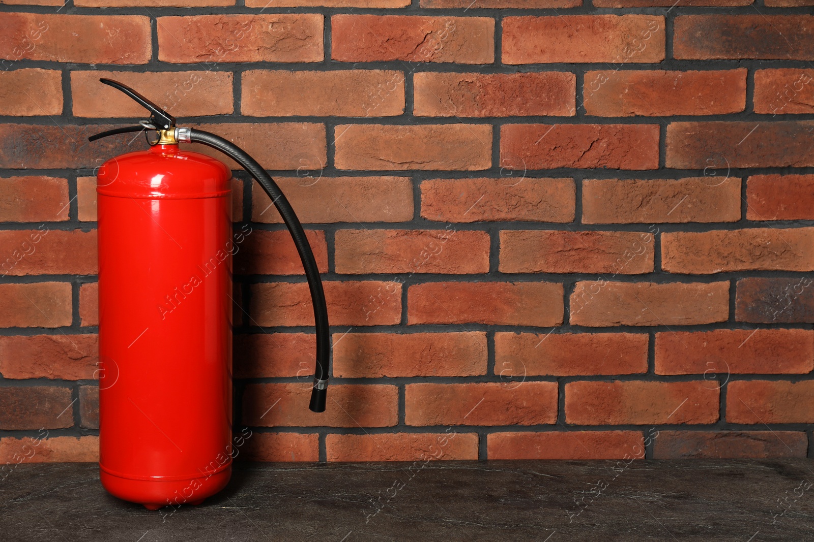 Photo of One red fire extinguisher near brick wall, space for text