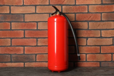 Photo of One red fire extinguisher near brick wall